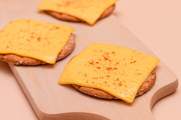 Crispy Cracker Sandwiches with Cheese and Paprika on Wooden Cutting Board and Beige Background