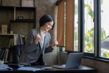 Happy asian bussiness woman celebrating victory while receiving good news on her labtop, excited...