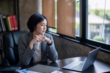 Thoughtful woman sitting at desk in front of laptop. Working on project and thinking on ideas.
