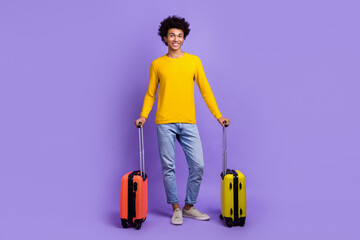 Full size photo of cheerful positive guy dressed yellow long sleeve jeans hold baggage in airport isolated on purple color background