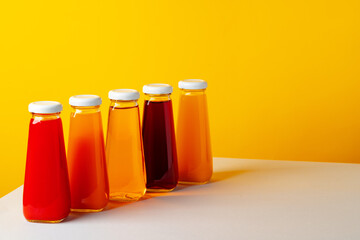 Glass bottle with juice on white table against yellow background