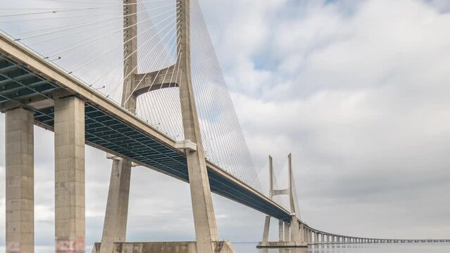 Architectural landmark Vasco da Gama Bridge over the Tagus River in Lisbon, Portugal. Green lawn with trees and cloudy sky. The longest bridge in the European Union.