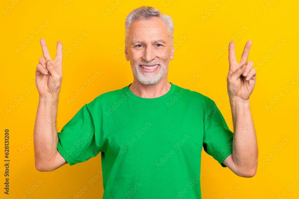 Poster Photo of positive funky guy dressed green t-shirt showing two v-signs isolated yellow color background