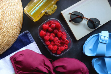 Maroon swimsuit, striped towel, straw hat, cactus cup with orange soda, bowl of raspberries, blue...