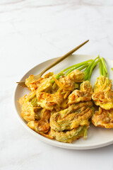 Fried zucchini flowers in batter, plate with zucchini flowers on marble background