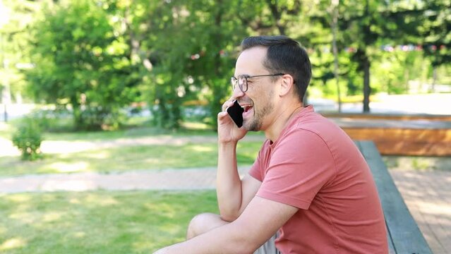 A man uses a phone, communicates cheerfully with friends, laughs, outdoors in a park on a summer day.