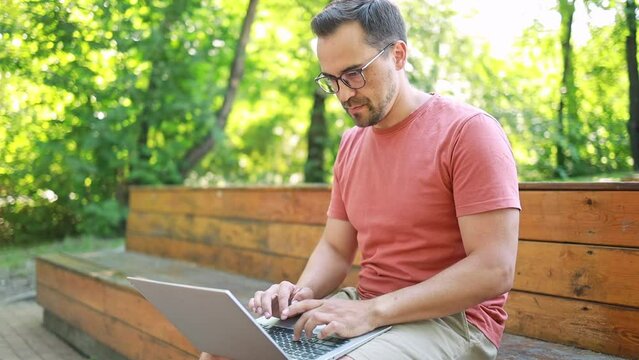A man is typing text on a laptop, in a park on a summer day. Distance learning online education and work