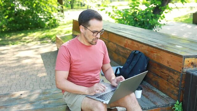 A man works remotely, uses a laptop, in the park on a summer day. Distance learning online education and work