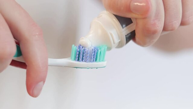 Squeezing toothpaste on a toothbrush, close-up. Brush your teeth. Health care, dental hygiene. A woman in the bathroom is squeezing white toothpaste out of a tube