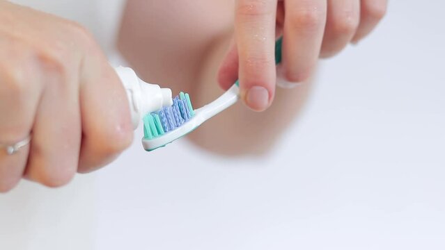 Squeezing toothpaste on a toothbrush, close-up. Brush your teeth. Health care, dental hygiene. A woman in the bathroom is squeezing white toothpaste out of a tube