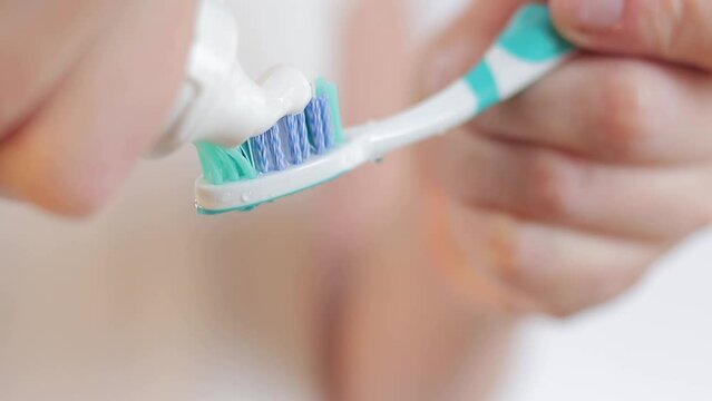 Squeezing toothpaste on a toothbrush, close-up. Brush your teeth. Health care, dental hygiene. A woman in the bathroom is squeezing white toothpaste out of a tube