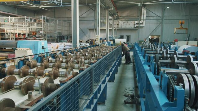 Engineers near metal sheet forming machine in metalwork factory. Steel rollers in metalforming machine for production roof tile in factory
