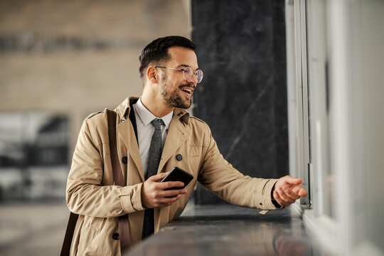A happy trendy businessman is buying train ticket at the station.
