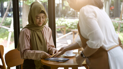 An upwardly mobile Asian Muslim woman enjoying a relaxing moment in the coffee shop on a bright sunny day