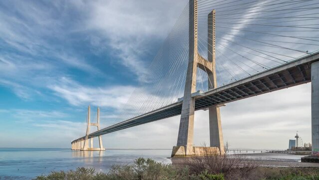 Vasco da Gama bridge timelapse hyperlapse with reflection on water and blue cloudy sky. Cable-stayed bridge and Tagus river. Lisbon, Portugal.