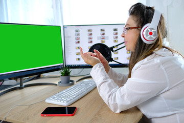 woman 40-45 years old, female blogger sits in front of computer with green screen in front of...