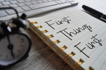 Close up image of alarm clock, keyboard and notebook with text FIRST THINGS FIRST.