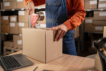 Worker man In Retail Warehouse working packing parcel box with tape dispenser for shipment....