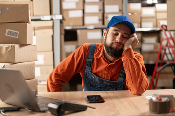 Young tired warehouse worker sleeping at workplace exhausted from overtime work