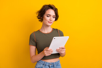 Photo of smart intelligent girl with bob hairstyle dressed khaki t-shirt look at tablet read email isolated on yellow color background