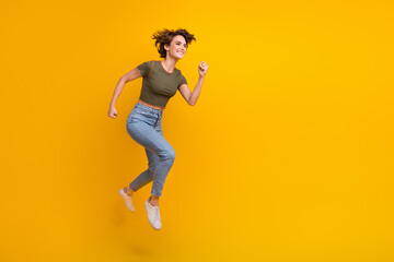 Fototapeta na wymiar Full length photo of pretty shiny lady wear khaki t-shirt jumping high running empty space isolated yellow color background