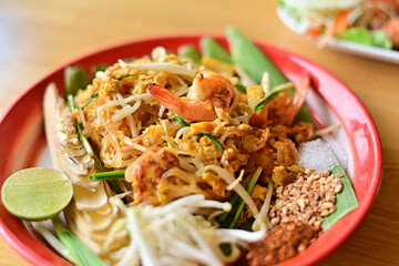 Pad Thai is placed on a brown wooden table. There is a woman squeezing lime juice to add more seasoning. Because Thai people like to eat spicy food. Famous Thai food concept. Street food. Thai identit