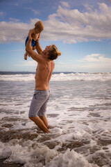 Father enjoying summer vacations, holding, playing and lifting his infant baby boy son high in the air on sandy beach. Family travel and vacations concept. Seminyak beach, Bali