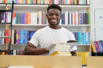 Smiling black guy with books in the library.