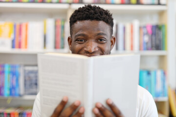 Positive African man with a book in his hands on the background of the library bookshelf.