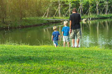 Back view of caucasian man use mobile phone to call about business and take care his son on vacation at waterside. Happy family outdoors resting together at waterfront. People enjoying nature outdoor.