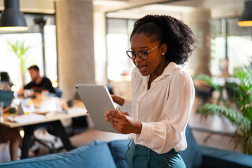 Upset African businesswoman in office. Young tired woman using digital tablet.