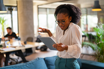 Upset African businesswoman in office. Young tired woman using digital tablet.