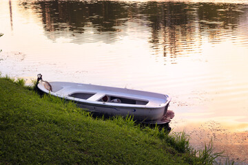 small rowing boat next to the shore, sunset on the river or lake, summer holidays and travel