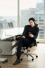 Portrait of confident serious asian businessman holding mobile phone working online, reading text message,  check email sitting in office chair. Technology, successful business concept  