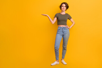 Fototapeta na wymiar Full length photo of cute funky lady wear khaki t-shirt holding arm empty space isolated yellow color background