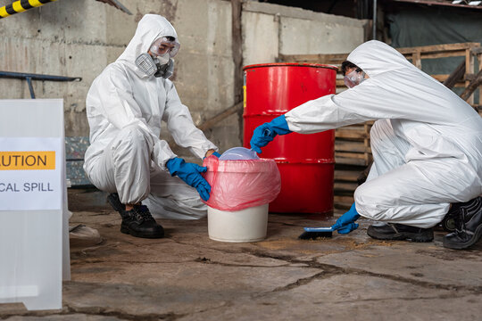 A team of two chemists, wearing PPE suits and gas masks, recover a deadly chemical spill on the factory warehouse floor. Correct disposal of chemical spills in industrial plants.