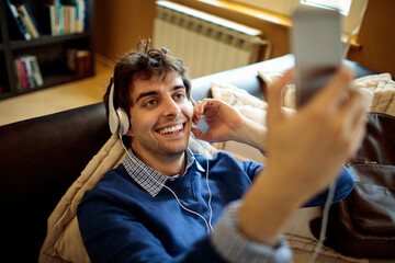 Young man listening to music on his smart phone while sitting on the couch in the living room