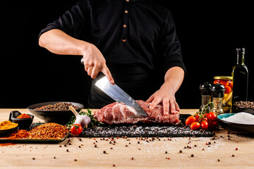 Chef cutting meat with a knife on kitchen table. Cooker is making a meal out of beef and vegetables on professional kitchen 