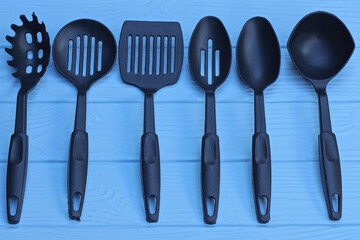 a set of six black plastic kitchen utensils lie on a blue wooden table