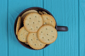 a pile of brown round cookies in a cup stands on a blue wooden table