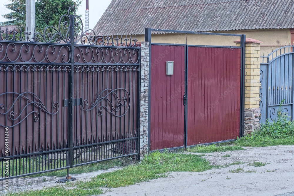 Sticker two large closed metal red and brown gates on a fence wall on a rural street