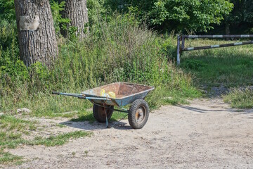 one empty old metal green rusty garden wheelbarrow stands on gray ground in the grass on a rural street