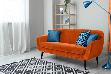 Interior of light living room with orange sofa, shelving unit and lamp