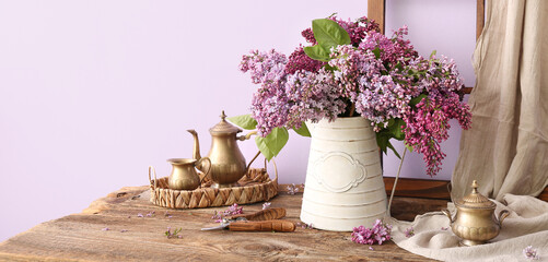 Composition with bouquet of lilac flowers and tea set on wooden table near wall