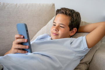 Relaxed casual boy using a smart phone lying on the couch at home