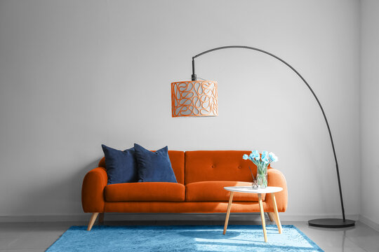 Interior of living room with orange sofa, floor lamp, table and blue carpet near white wall