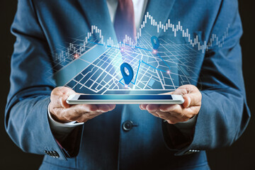 Businessman with tablet computer using virtual screen with digital city map, location pointers and chart on dark background. Navigation concept