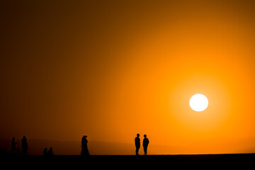 Fototapeta na wymiar Silhouette of tourists watching a spectacular sunset from a harbour wall (Chania, Crete, Greece)