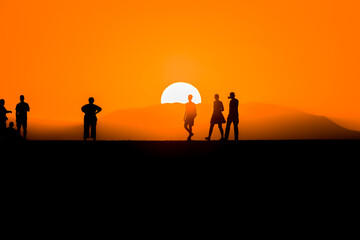 Silhouette of tourists watching the sun set behind a distant mountain in summer