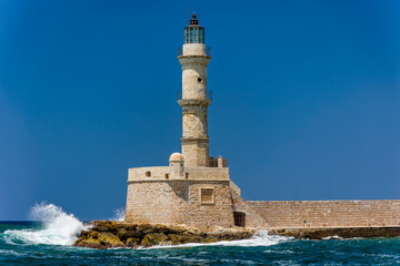 Waves breaking on a sea wall next to an old Venetian era lighthouse on a clear day